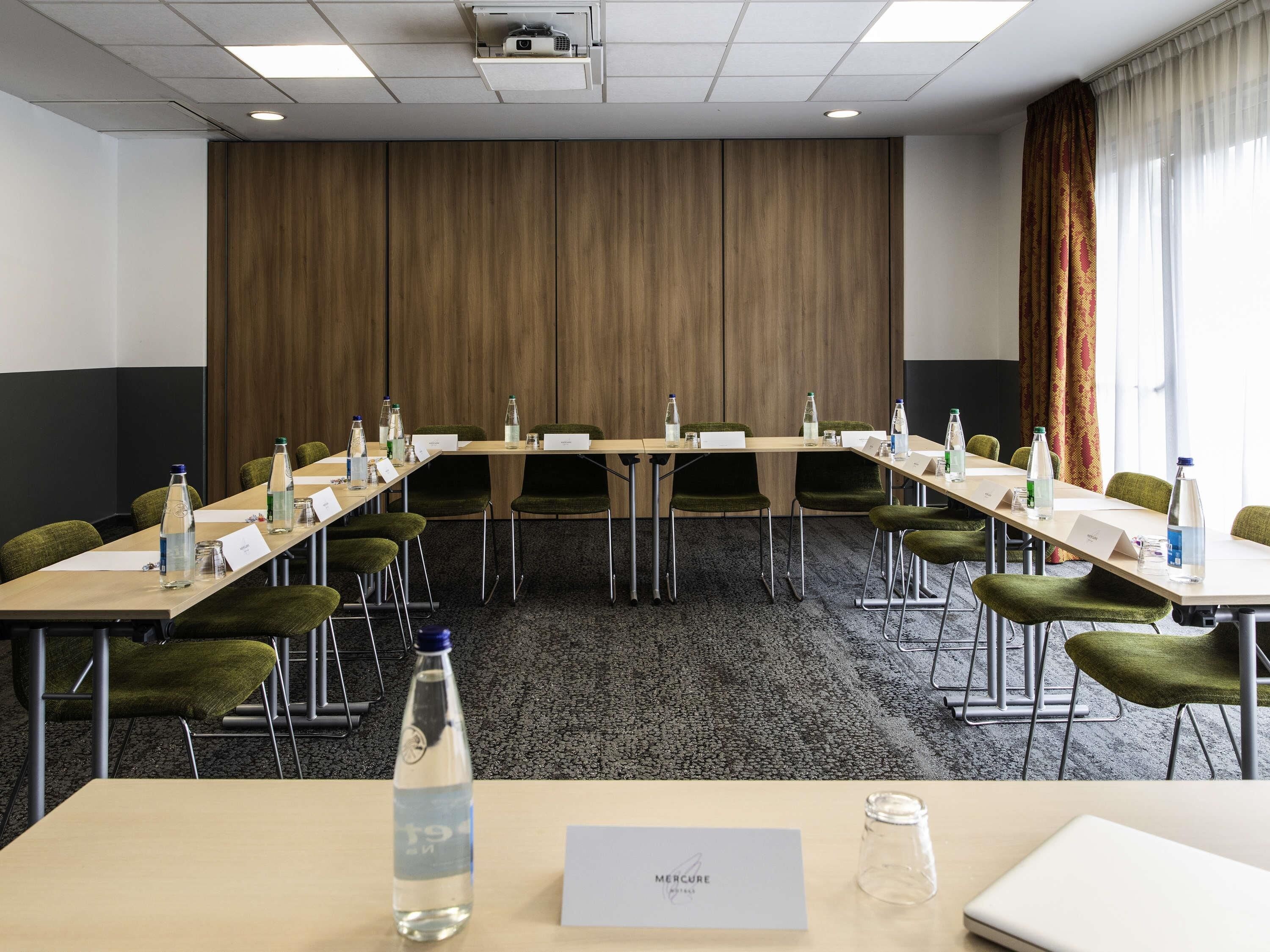 A conference room with a long table, chairs, name cards, water bottles, and a projector.