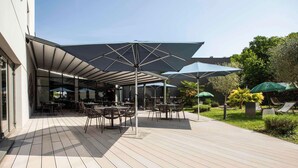 An outdoor patio area with tables and chairs, umbrellas, and a garden. - Mercure Belfort Centre (Belfort)