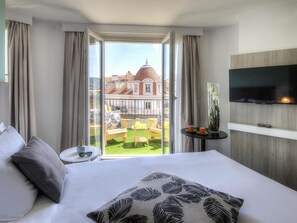 A hotel room with a bed, a TV, a balcony with a view of buildings, and a small table with a vase. - Ibis Styles Nice Centre Gare (Nice)
