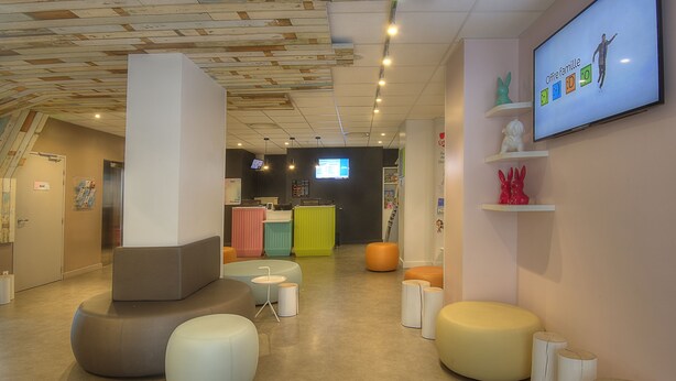 A modern interior with colorful seating, a reception area, and a TV displaying 'Offre famille'. - Ibis Styles Nice Centre Gare (Nice)