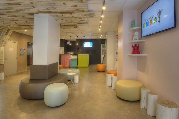 A modern interior with colorful seating, a reception area, and a TV displaying 'Offre famille'. - Ibis Styles Nice Centre Gare (Nice)