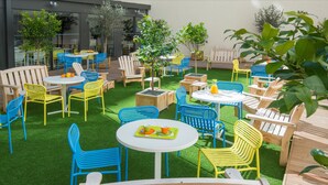 An outdoor patio area with multiple tables and chairs, surrounded by greenery and trees. - Ibis Styles Nice Centre Gare (Nice)