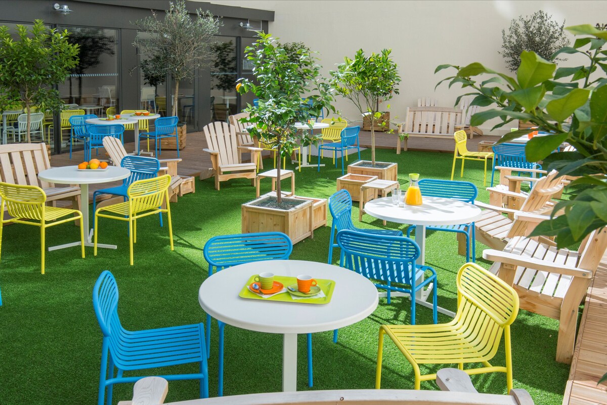 An outdoor patio area with multiple tables and chairs, surrounded by greenery and trees.