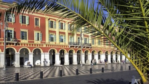 A courtyard with a checkered floor, palm trees, and a red building with columns and balconies. - Ibis Styles Nice Centre Gare (Nice)