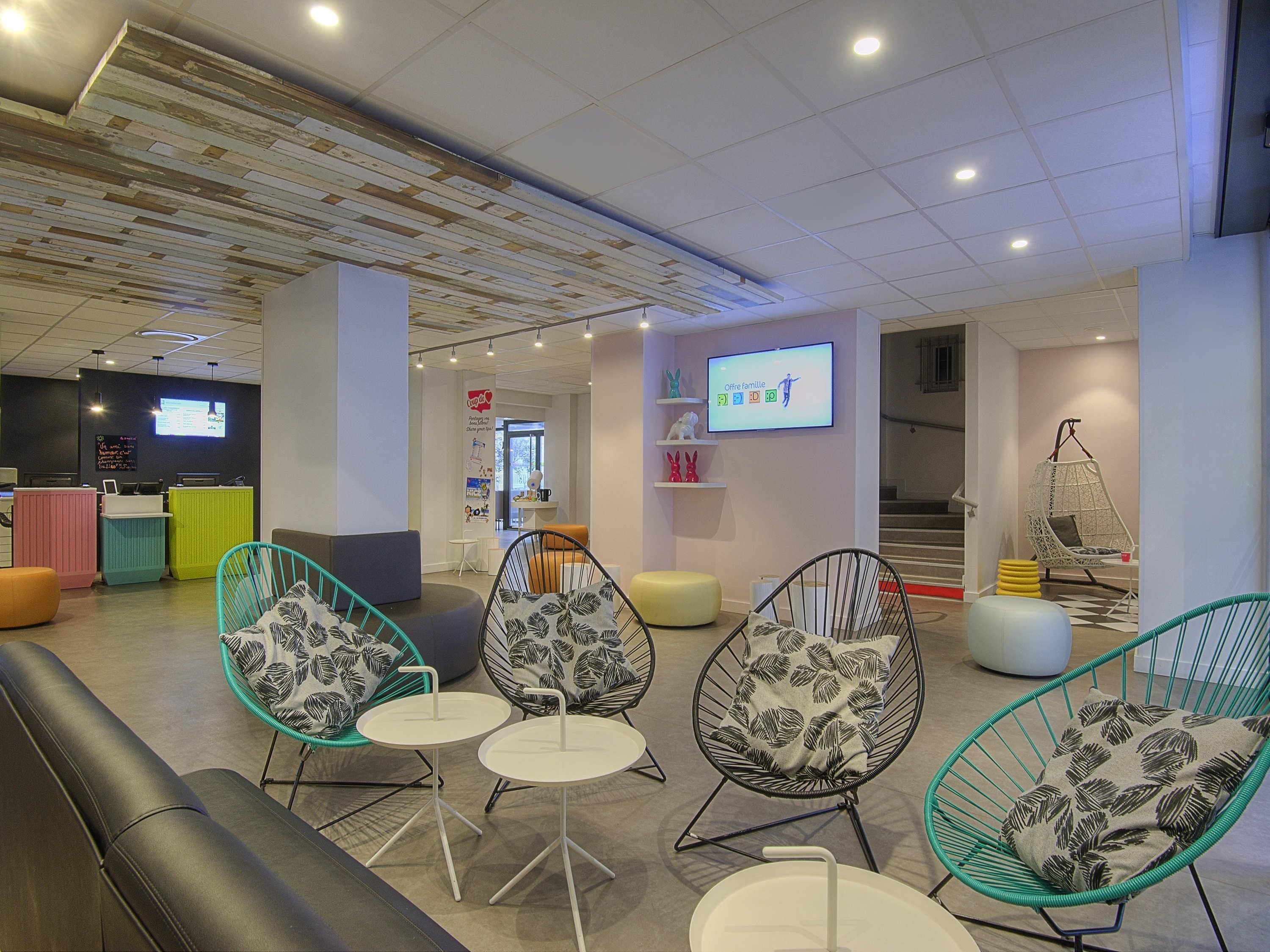 A modern lounge area with comfortable seating, a reception desk, and a TV screen displaying a family-oriented program.