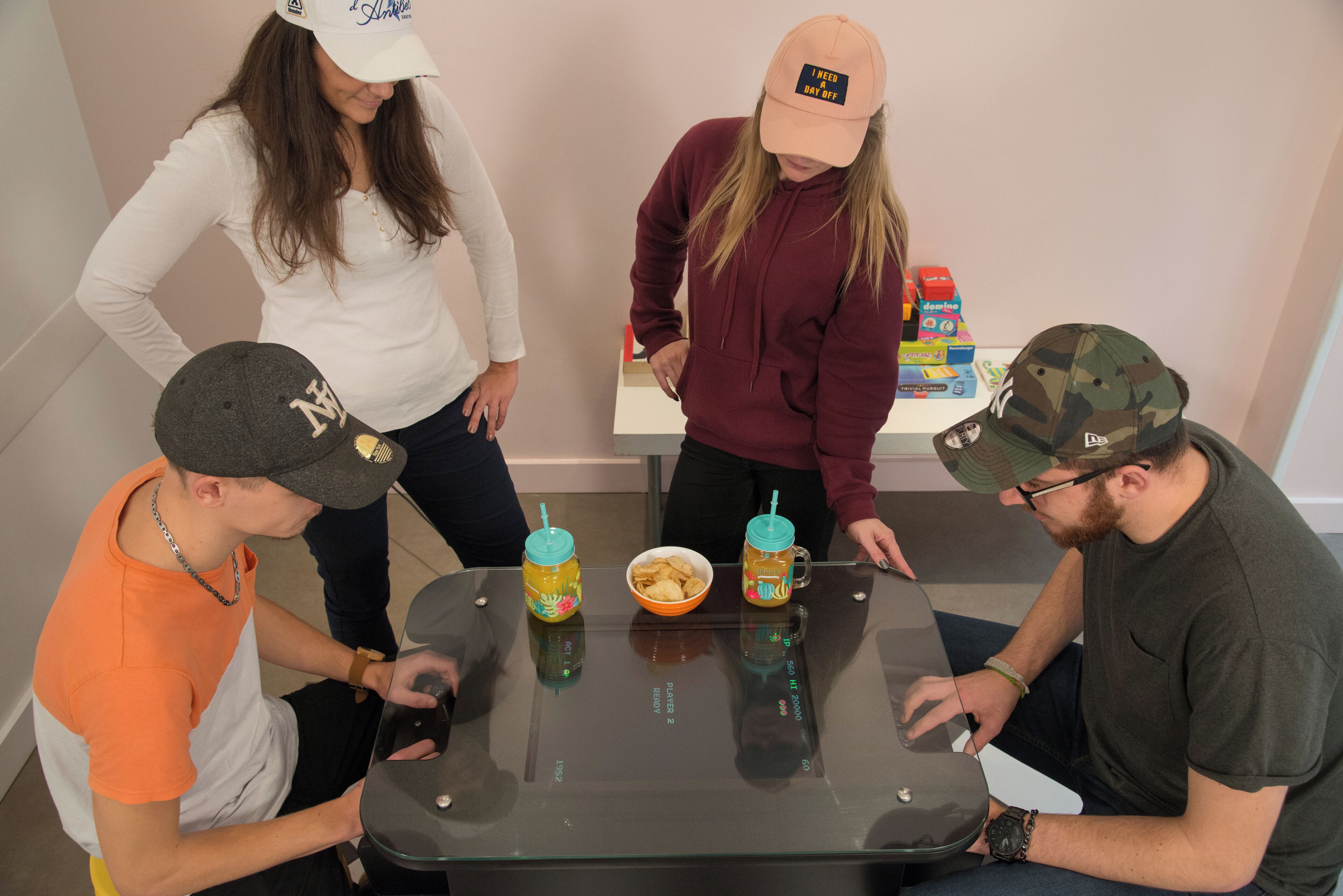 Four people around a table with a laptop, two drinks, and a bowl of chips.