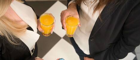 Two individuals holding glasses of orange juice, one holding a smartphone.