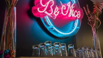 Un letrero de neón con el texto 'Be Nice' en un diseño circular, rodeado de botellas de vidrio transparentes.