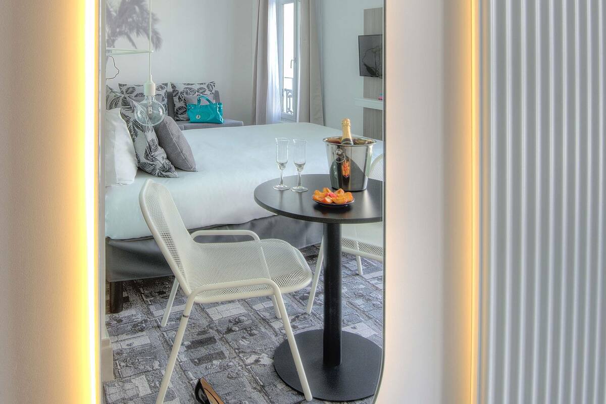A hotel room with a bed, a table with two glasses and a bottle of champagne, and a chair.