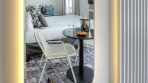A modern hotel room with a bed, a small round table with a bottle and glasses, a chair, and a pair of shoes on the floor. - Ibis Styles Nice Centre Gare (Nice)