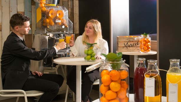 A man and a woman sitting at a table with a fruit juicer and various fruit containers. - Ibis Styles Nice Centre Gare (Nice)