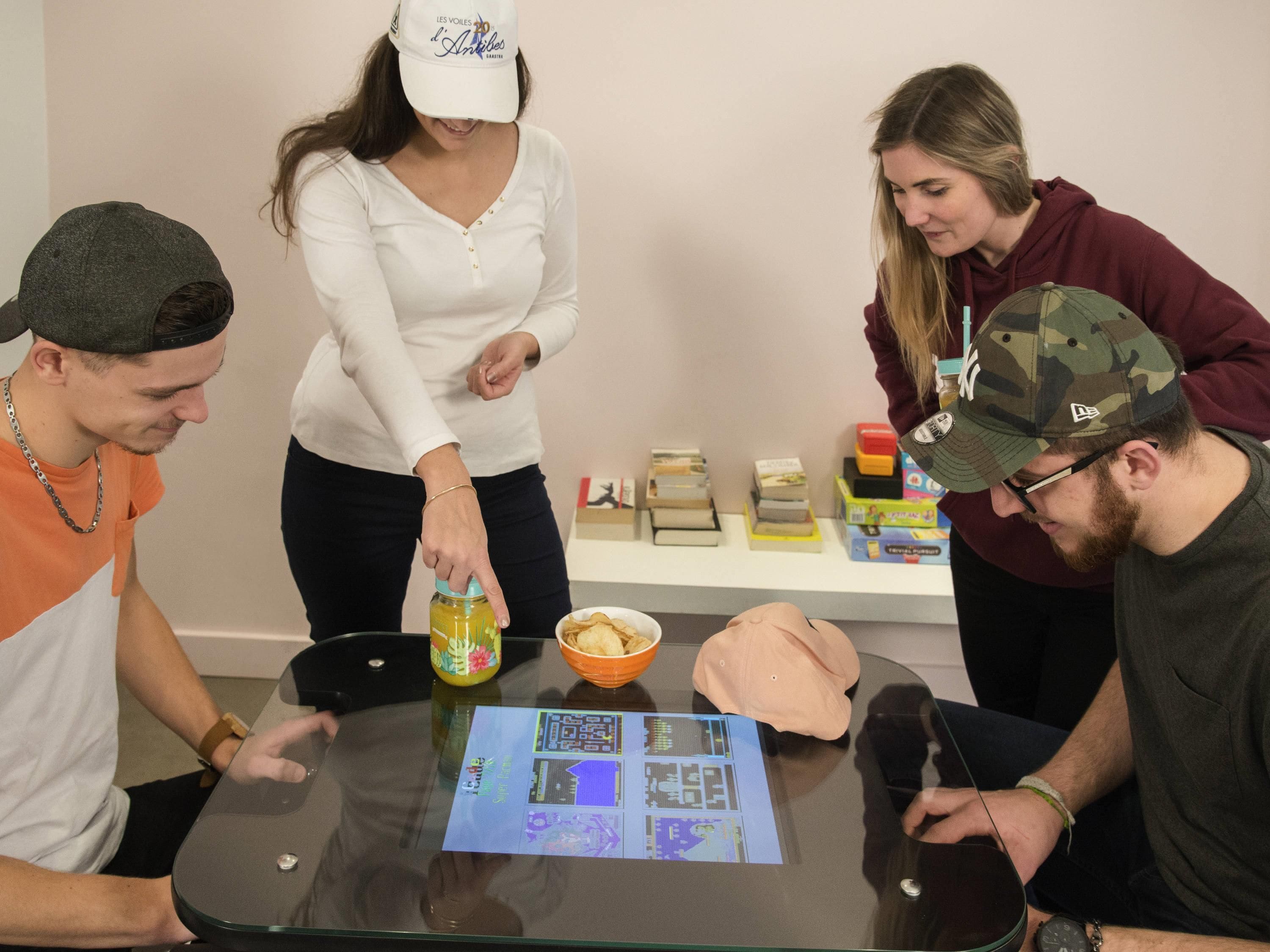 A group of people around a table with a game board, a bowl of chips, and a bottle of juice.