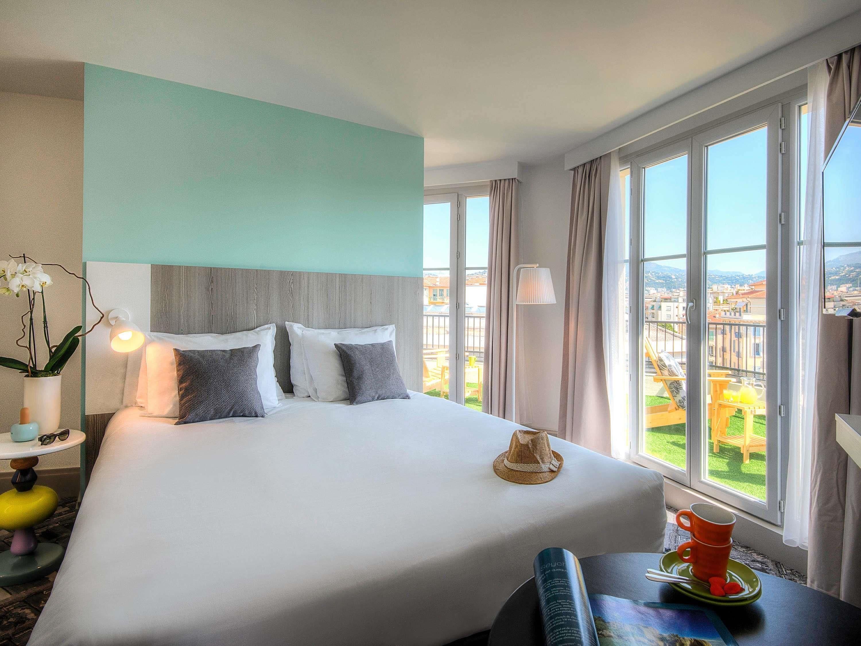 Habitación de hotel con una cama grande, vistas de la ciudad y un balcón con mesa y sillas.