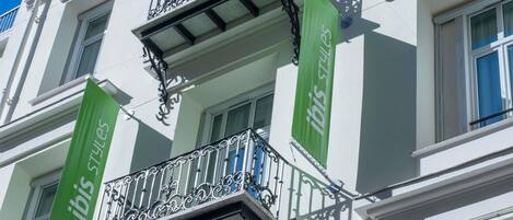 Un edificio con balcón que presenta barandillas de metal negro ornamentadas y un estandarte verde con el texto 'ibis styles'.