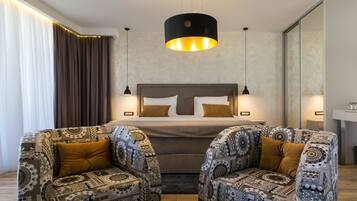 Ein modernes Hotelzimmer mit einem großen Bett, zwei gemusterten Sessel, einem Glastisch und einer Pendelleuchte darüber.