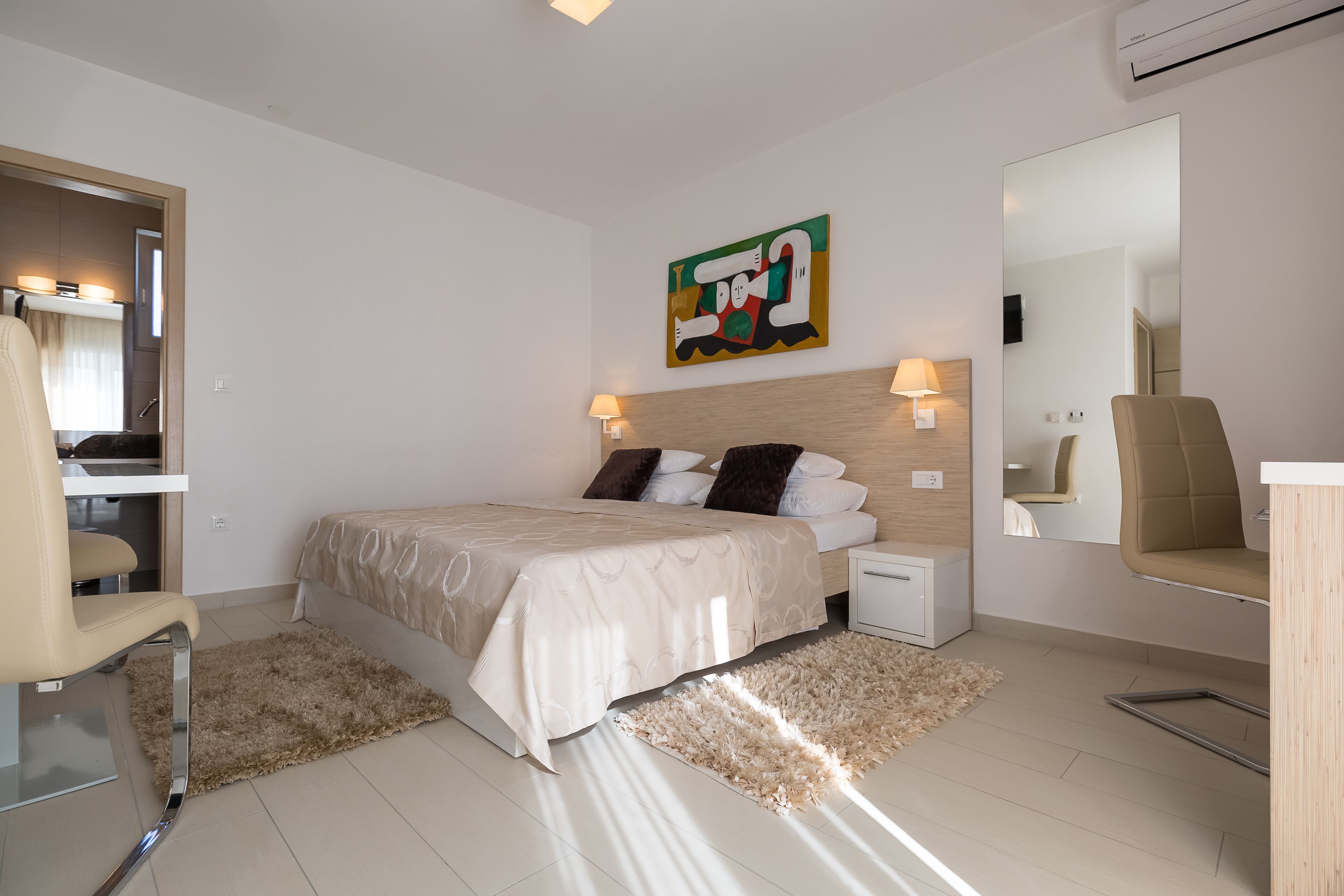 Une chambre d’hôtel moderne, équipée d’un lit, de tables de chevet, d’une chaise, d’un miroir et d’un tableau au mur.