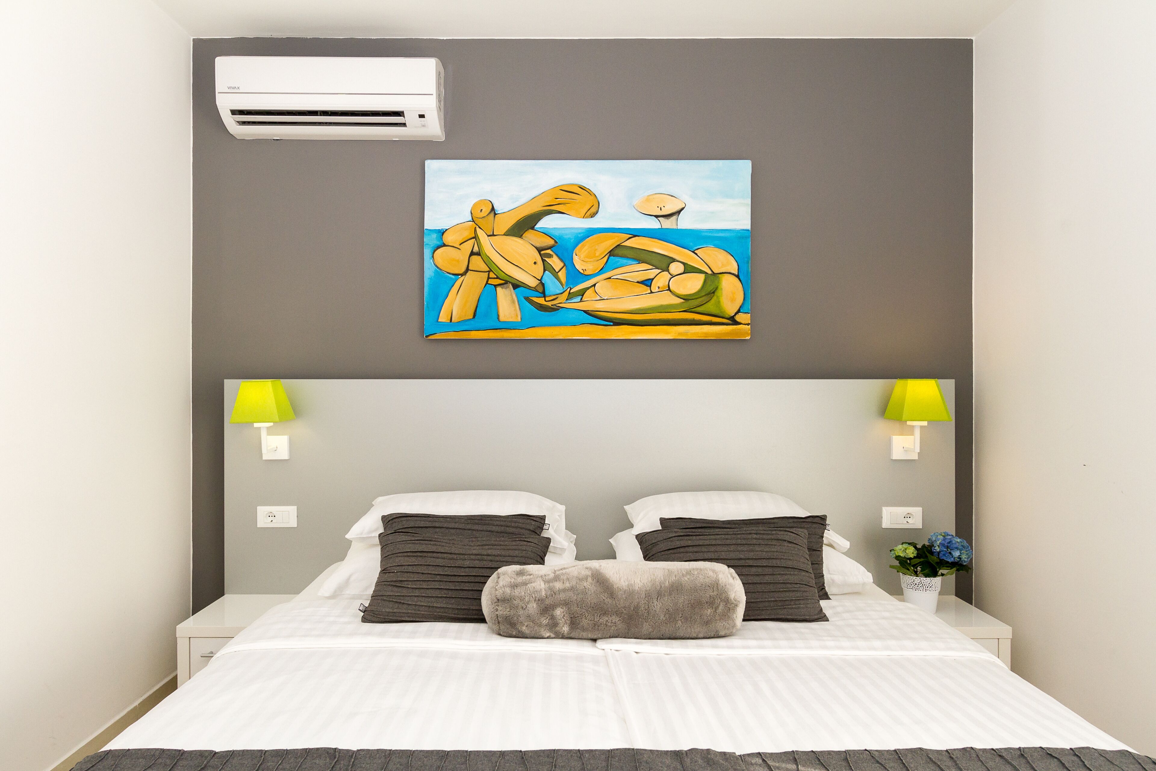 Una habitación de hotel con una cama, dos lámparas de noche, un cuadro y un aire acondicionado de pared.