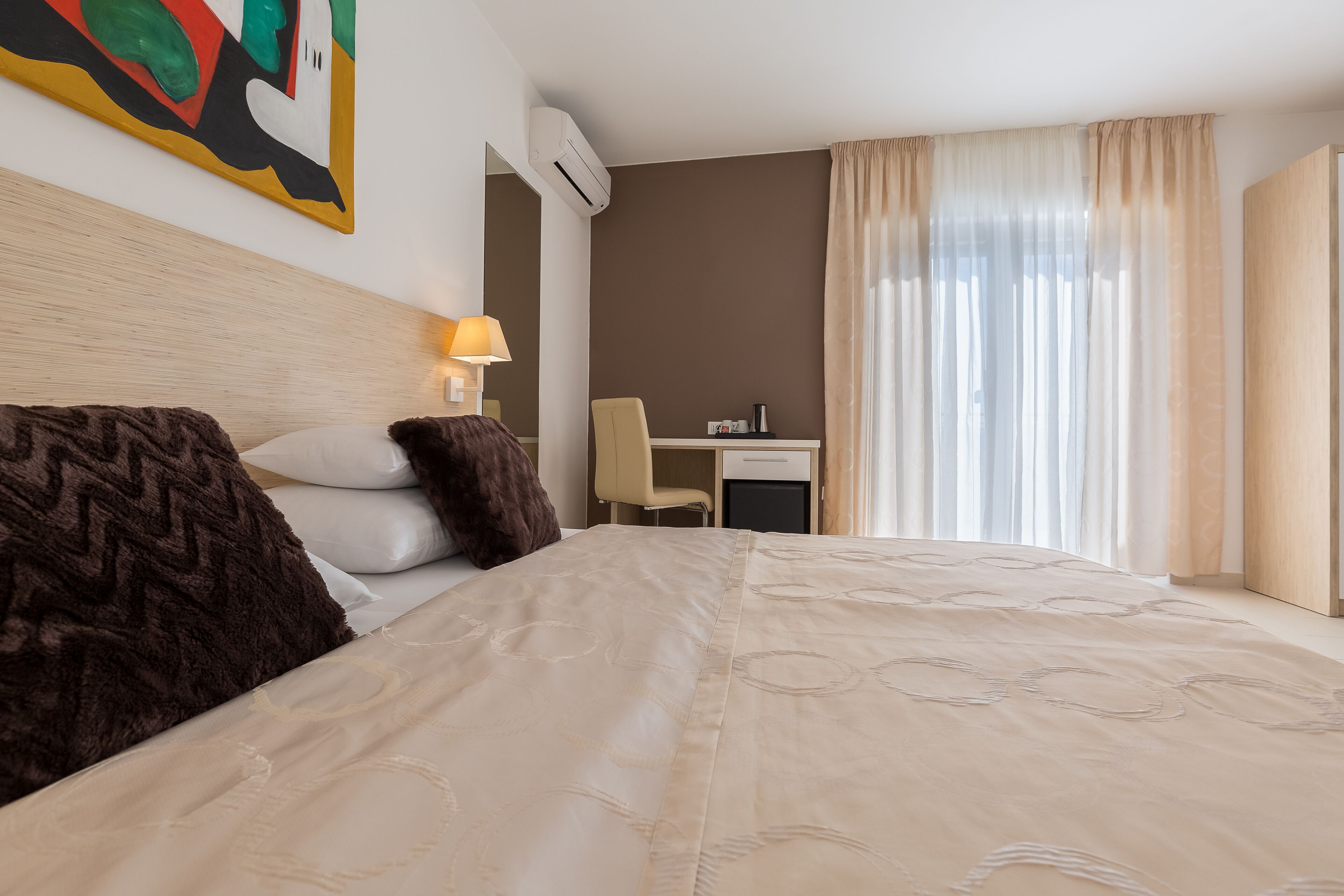 Une chambre d’hôtel avec un grand lit, un bureau, une chaise, une lampe et une fenêtre avec des rideaux.