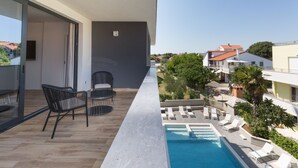 En balkon med pool, liggestole og et spiseområde med stole og bord.