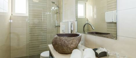 A modern bathroom with a glass shower enclosure, a large stone sink, and a mirror above the sink.