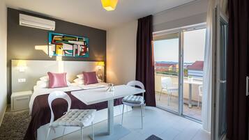 Una habitación de hotel moderna con una cama, dos sillas blancas, una mesa de comedor y un balcón con vistas.