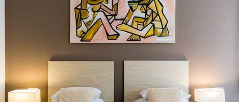A hotel room with two beds, each with a lamp and a pillow.