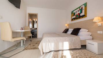 A modern hotel room with a bed, a desk, a chair, a TV, and a painting on the wall.