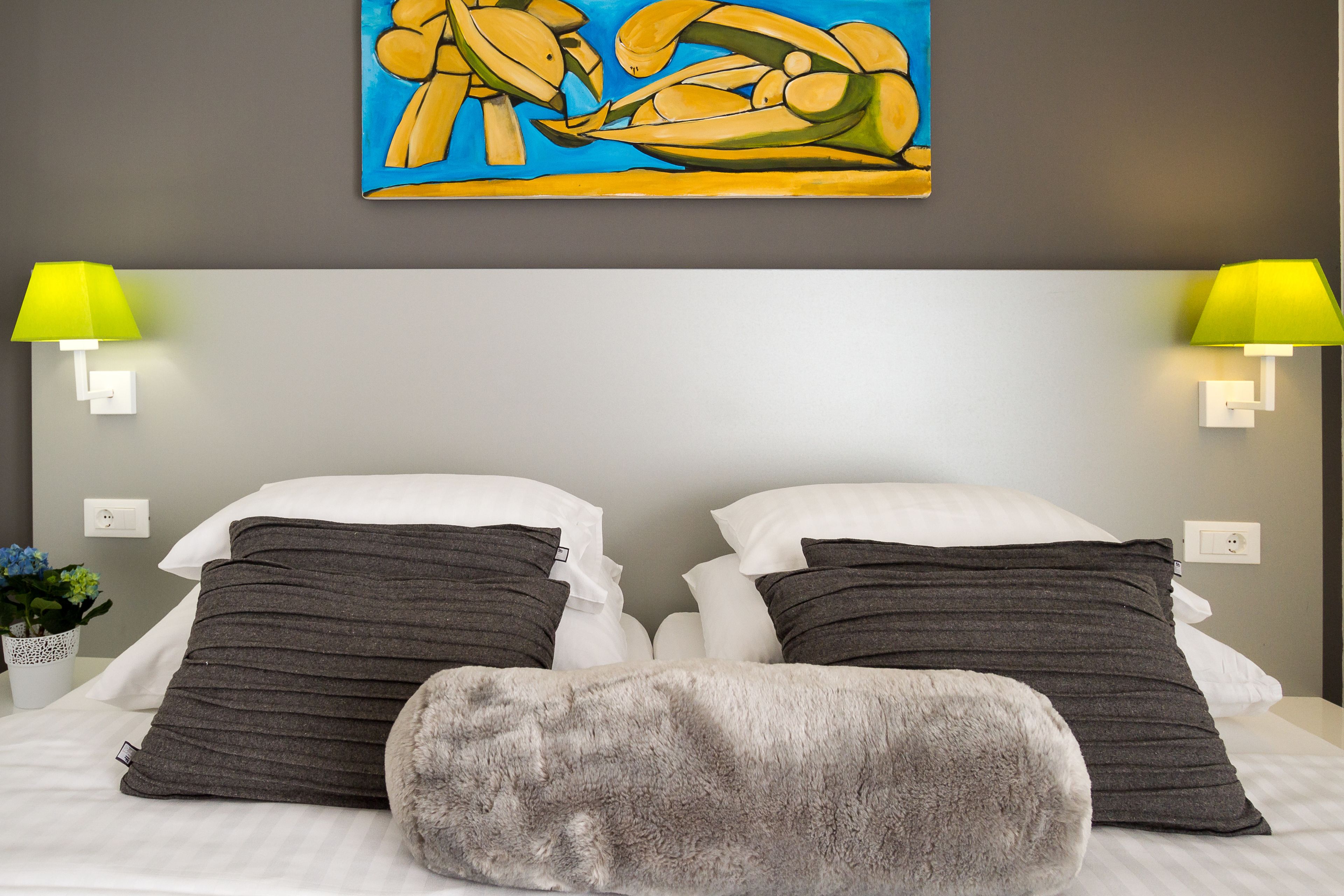 A neatly made bed with two pillows, a fluffy throw, and a painting above.