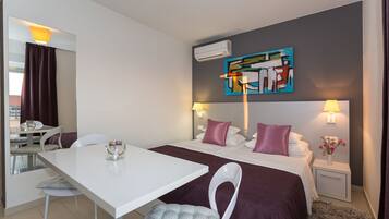 A hotel room with a bed, bedside tables, a desk, chairs, and a painting on the wall.