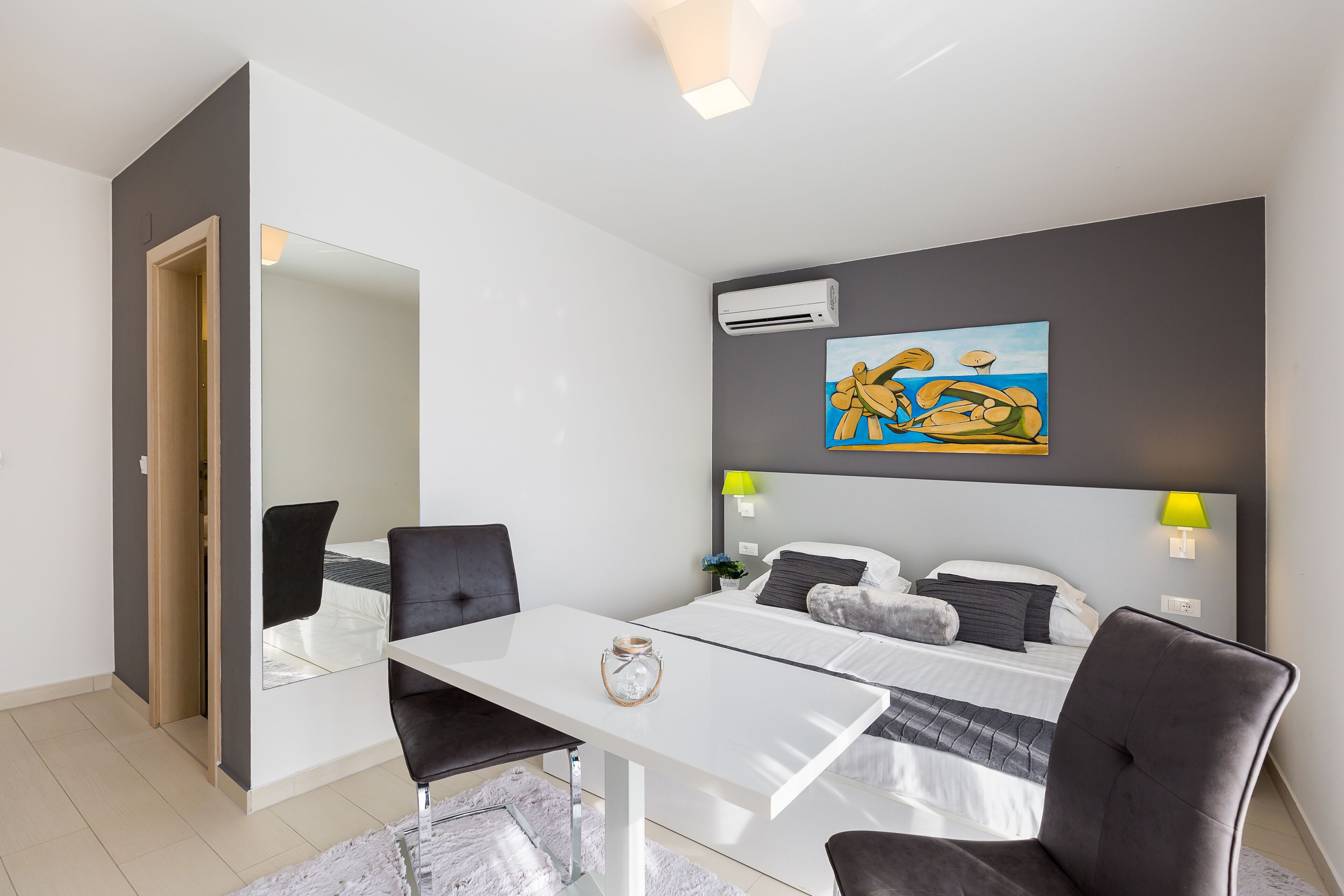 A modern hotel room with a bed, bedside lamps, a desk, and a large mirror.