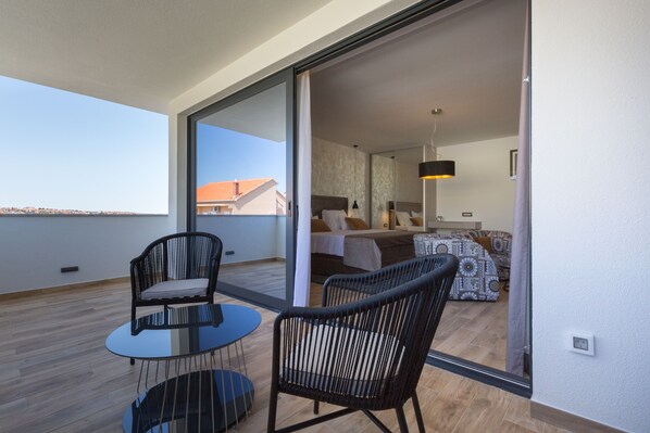 Un balcón con puerta de cristal que da a un dormitorio con cama, una silla y una mesa.