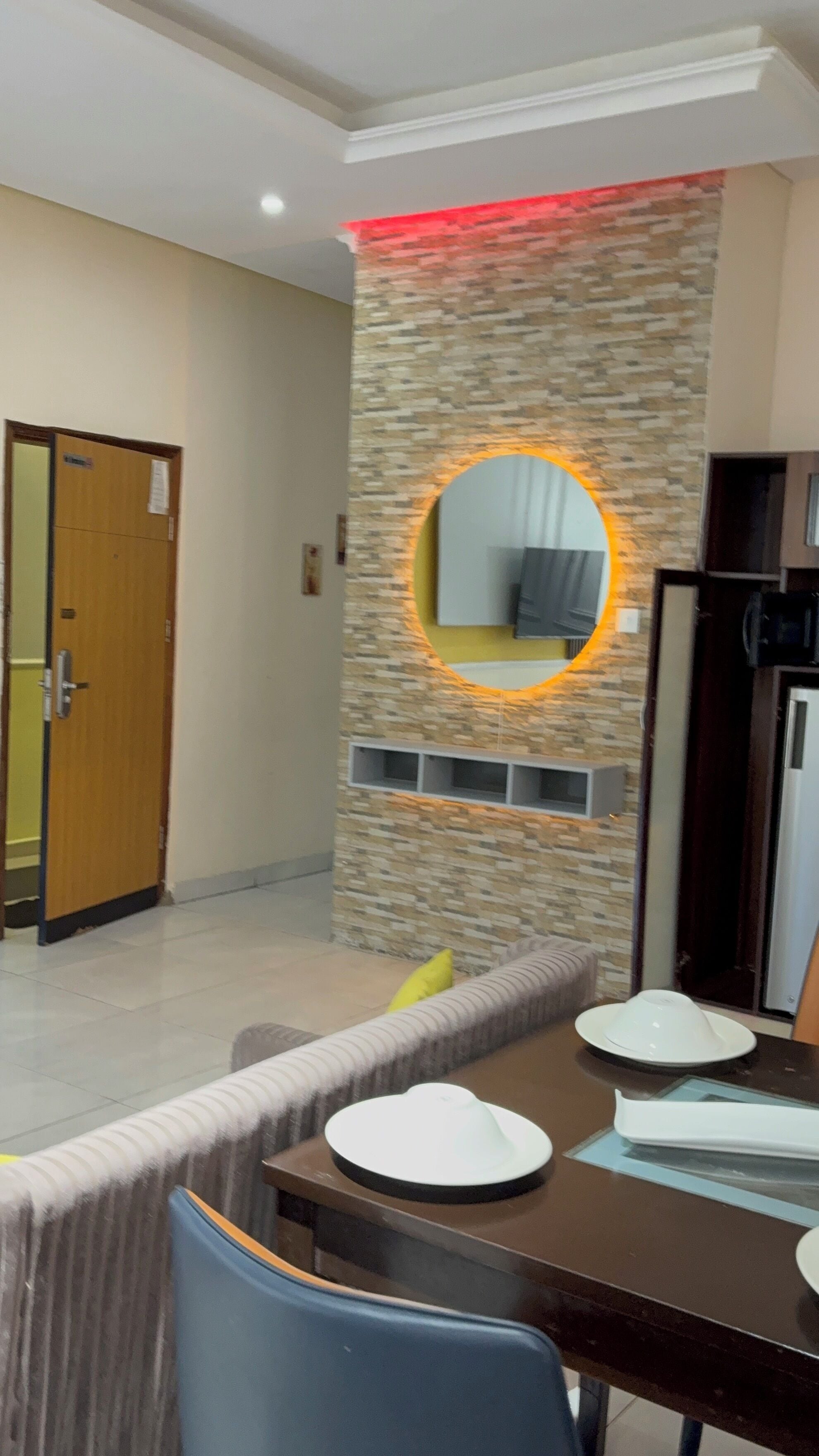 A dining area with a stone wall, a round mirror, and a dining table with chairs.