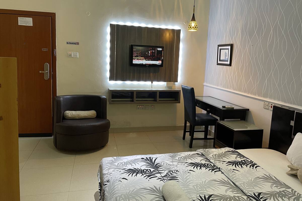 A hotel room with a bed, a desk, a chair, a TV mounted on the wall, and a door.