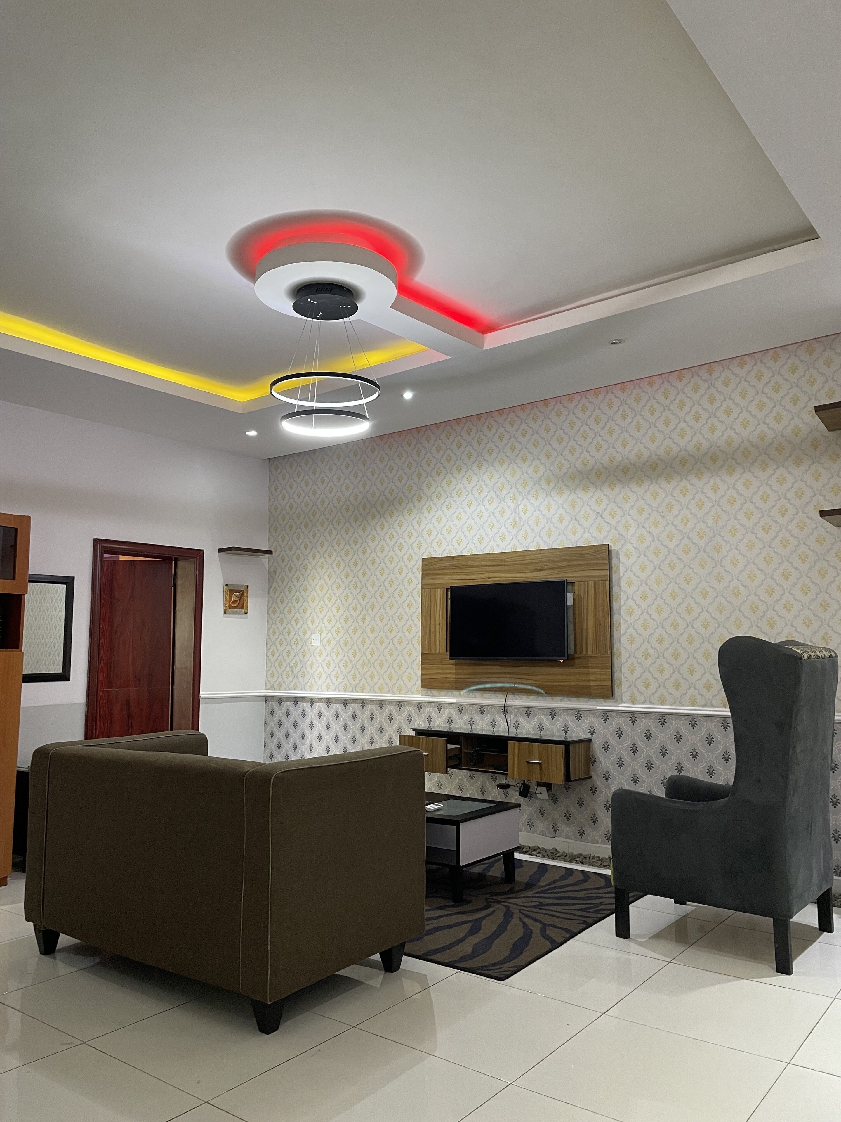 Una sala de estar moderna con un sofá, un sillón, un televisor montado en la pared e iluminación empotrada en el techo.