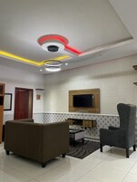 Una sala de estar moderna con un sofá, un sillón, un televisor montado en la pared e iluminación empotrada en el techo.