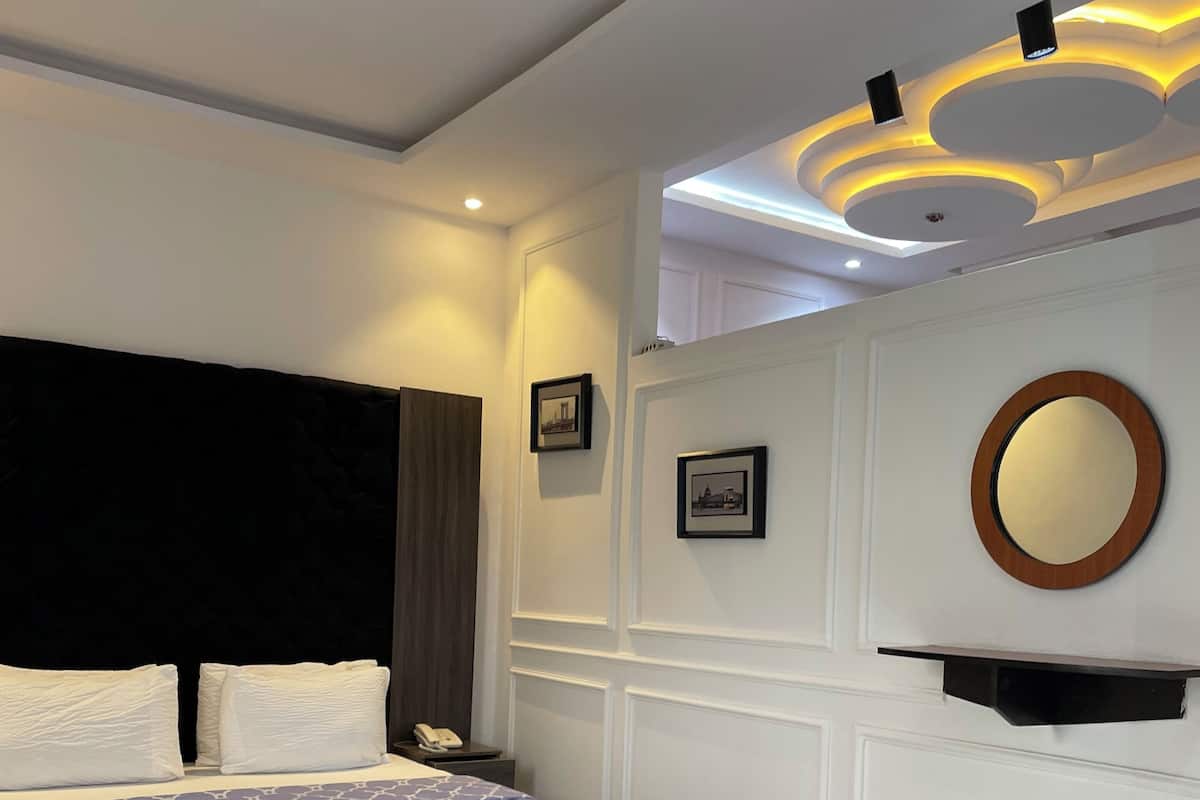 A modern bedroom with a large bed, a grey ottoman, a round mirror, and framed pictures on the wall.