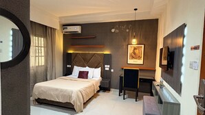 Una habitación de hotel moderna con una cama grande, un escritorio, un televisor de pantalla plana y un equipo de aire acondicionado.