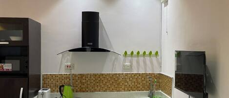 A modern kitchen with dark cabinets, a countertop, a stove, and a wall-mounted TV.