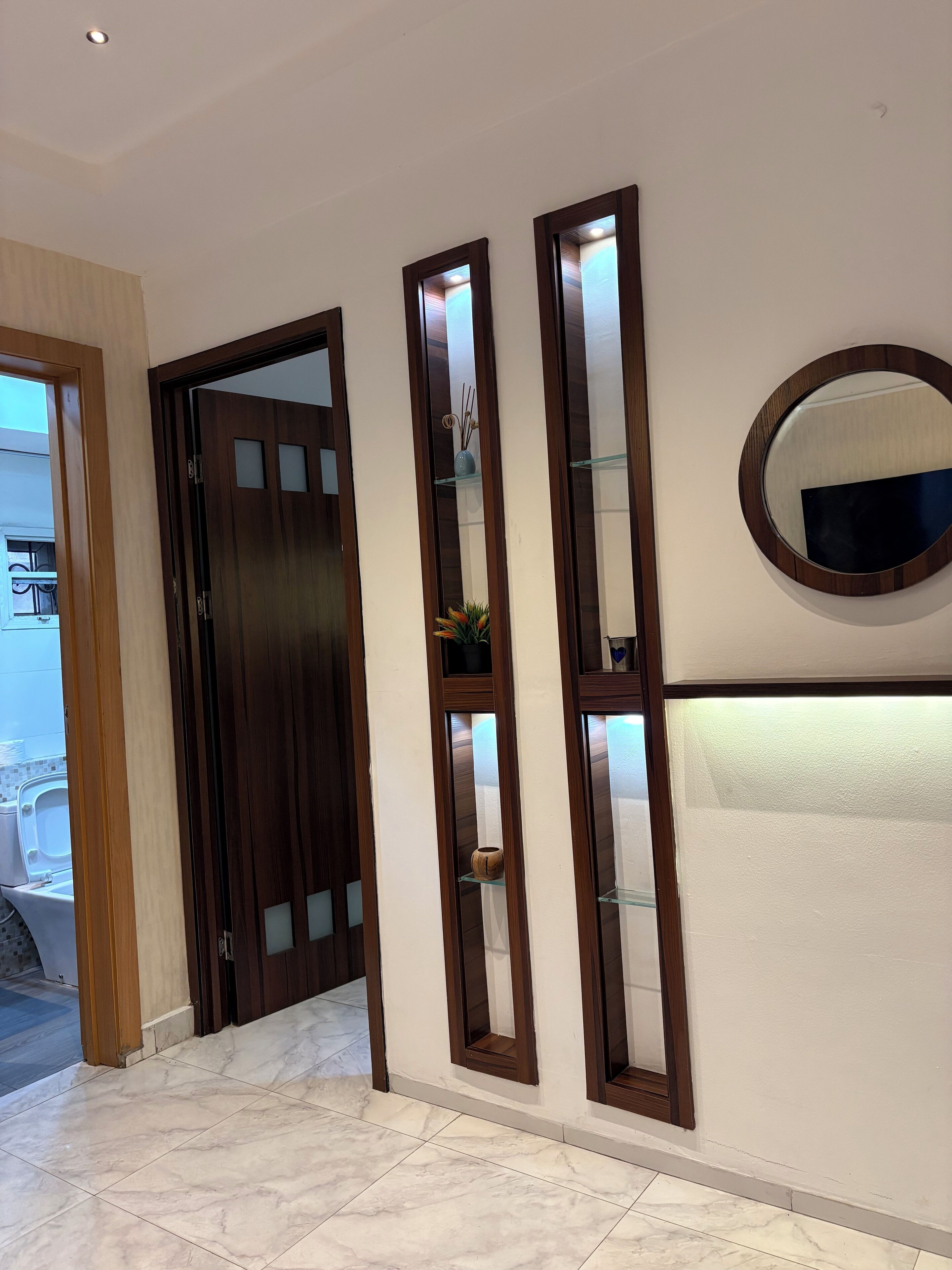 Un pasillo con puerta de madera, un espejo y estantes con adornos.