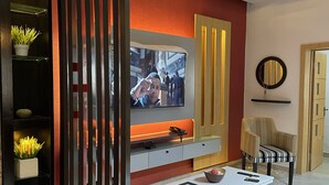 Una sala de estar moderna con televisor, un reposapiés rojo y un techo decorativo.
