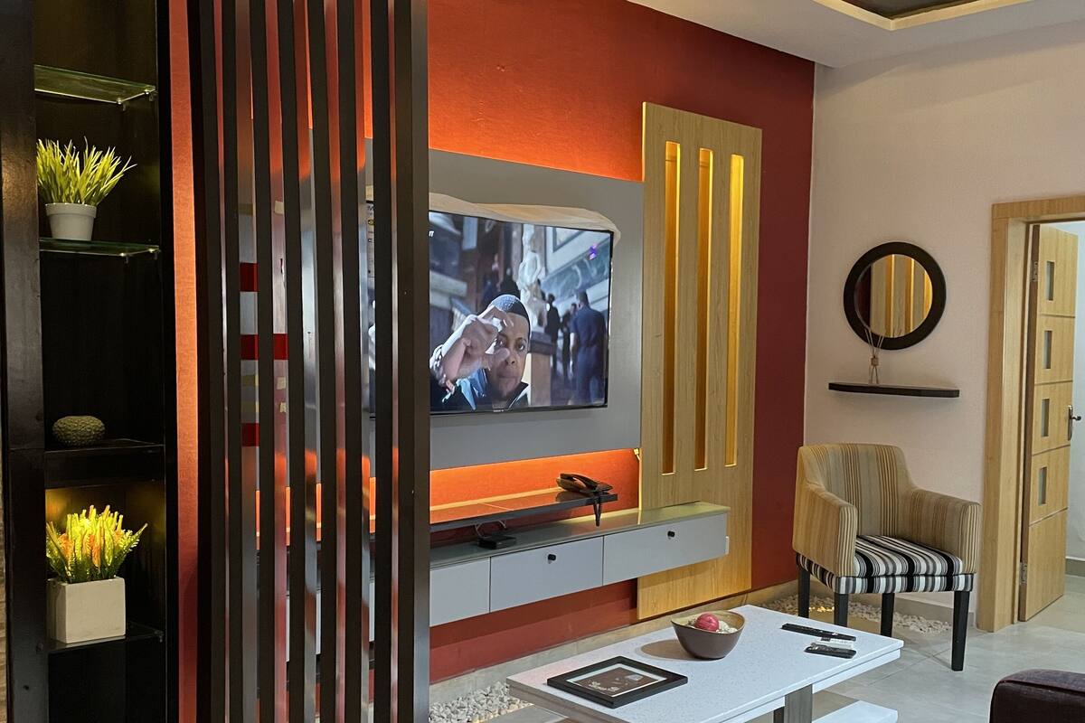 A modern living room with a TV, red ottoman, and a decorative ceiling.