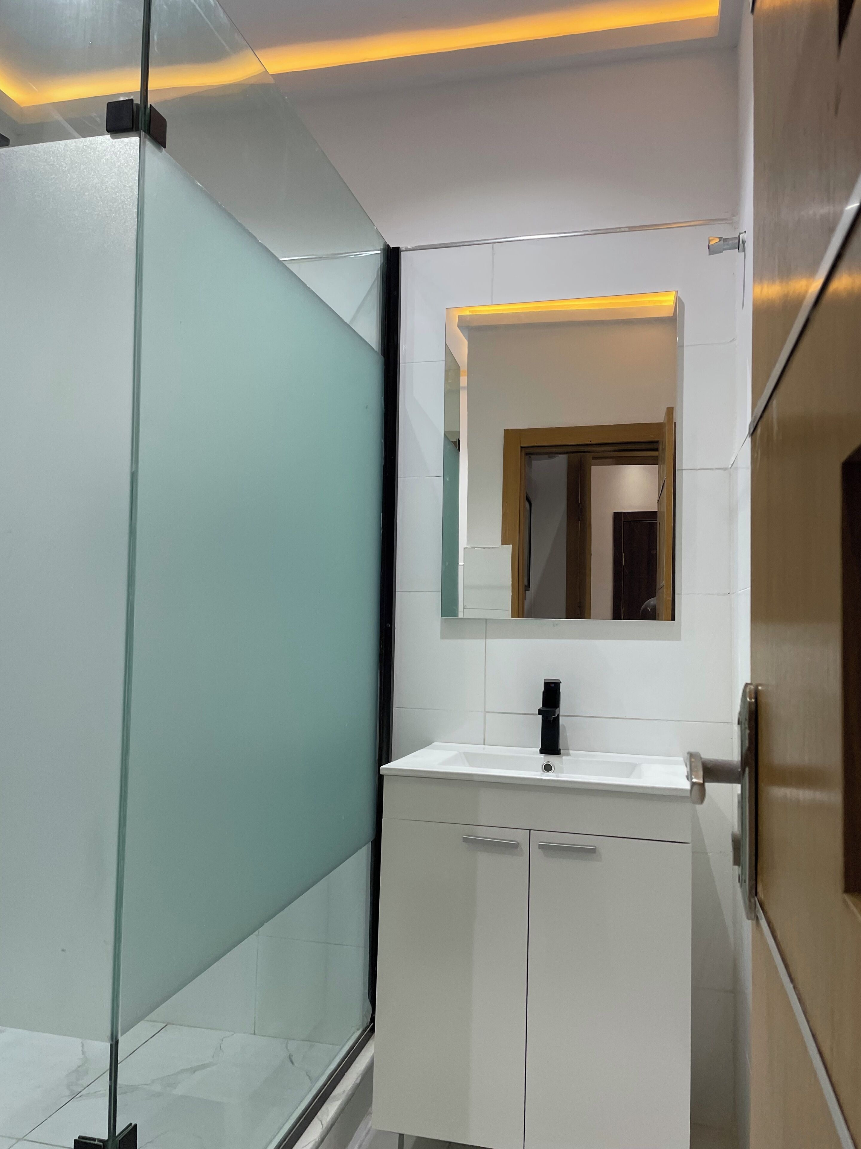 A modern bathroom with a glass shower enclosure, a white vanity with a black faucet, and a mirror above the sink.