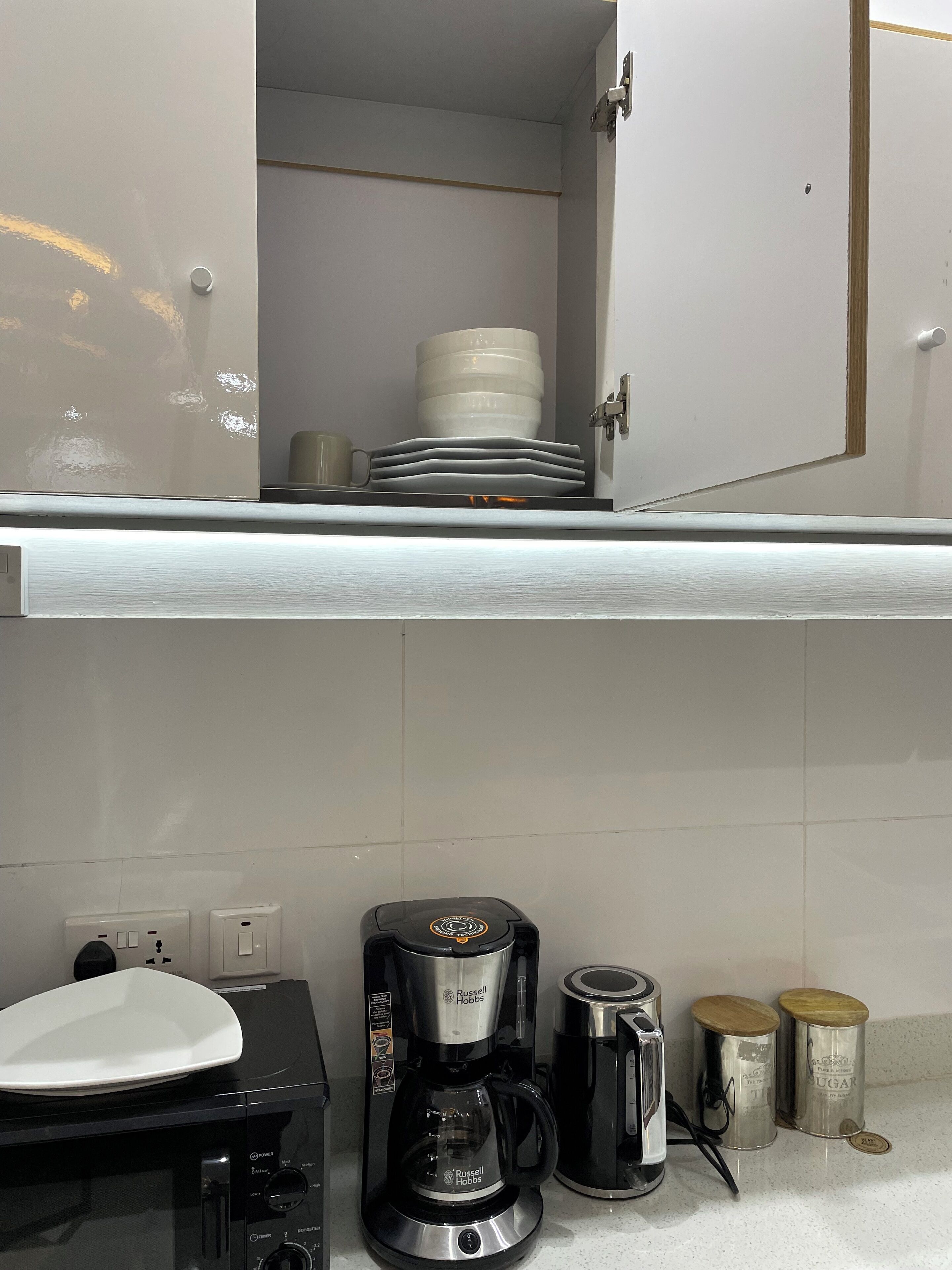 A kitchen with a coffee maker, a microwave, and a toaster. There are also two containers on the counter.