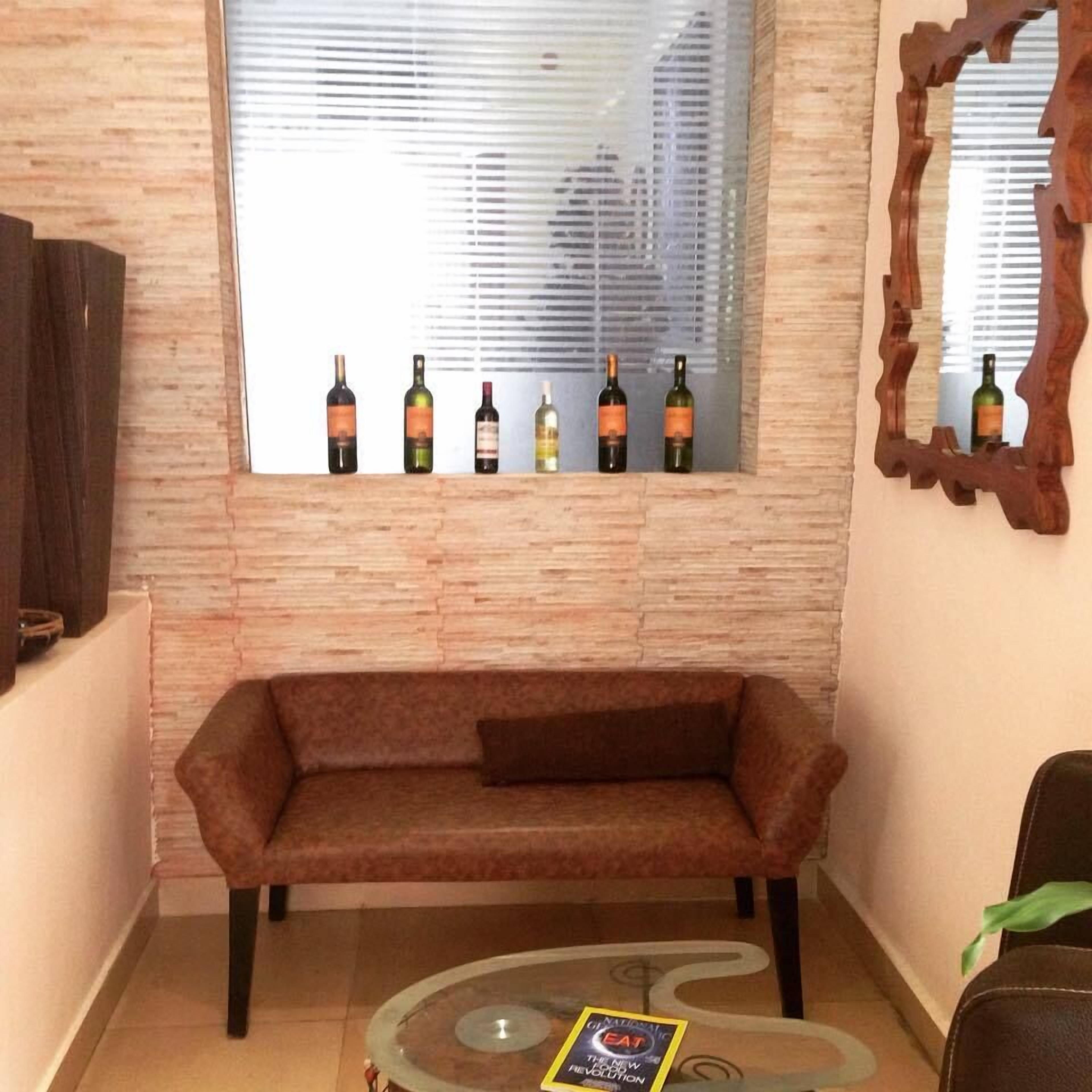 A living room with a sofa, a coffee table, and a window with bottles of wine.