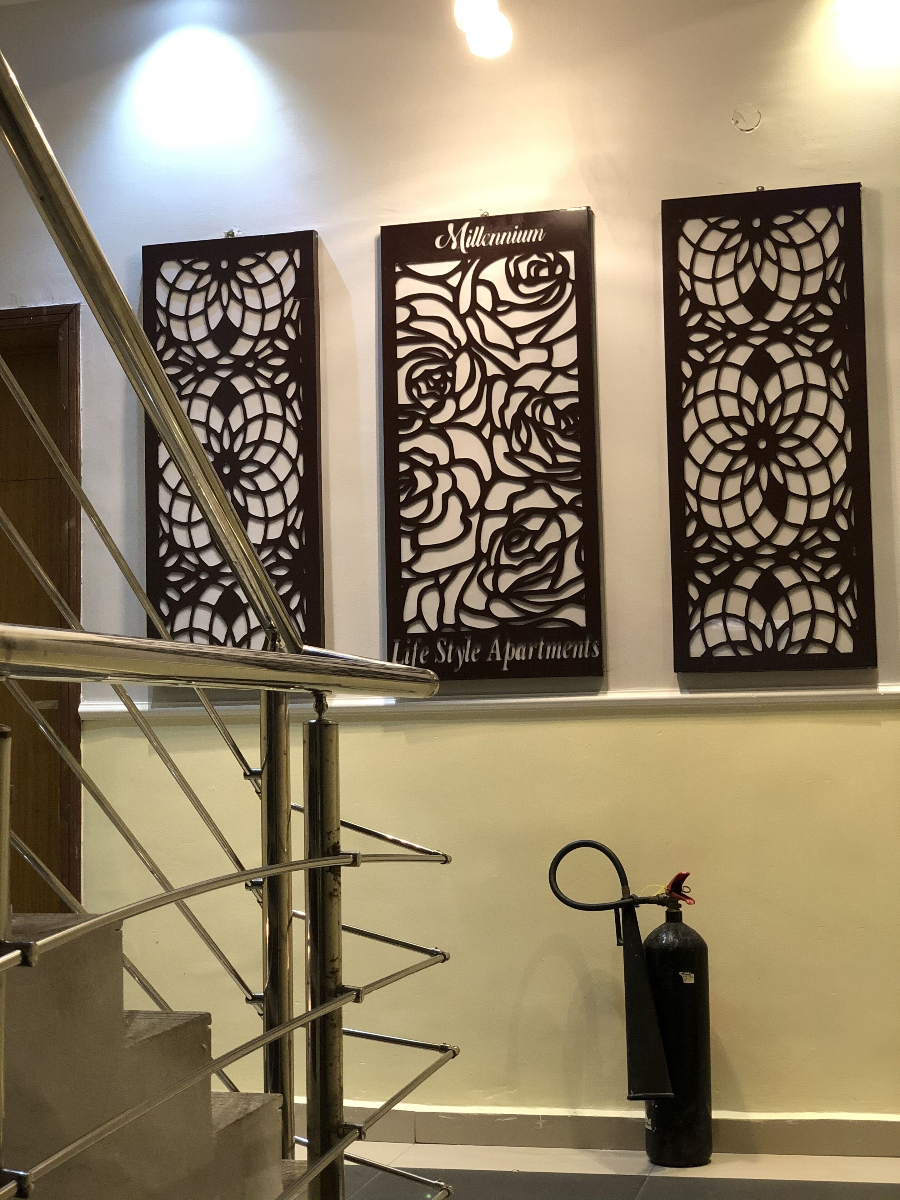 Een trap met metalen leuningen, een aan de muur bevestigd blusapparaat en decoratieve panelen met bloemmotieven.