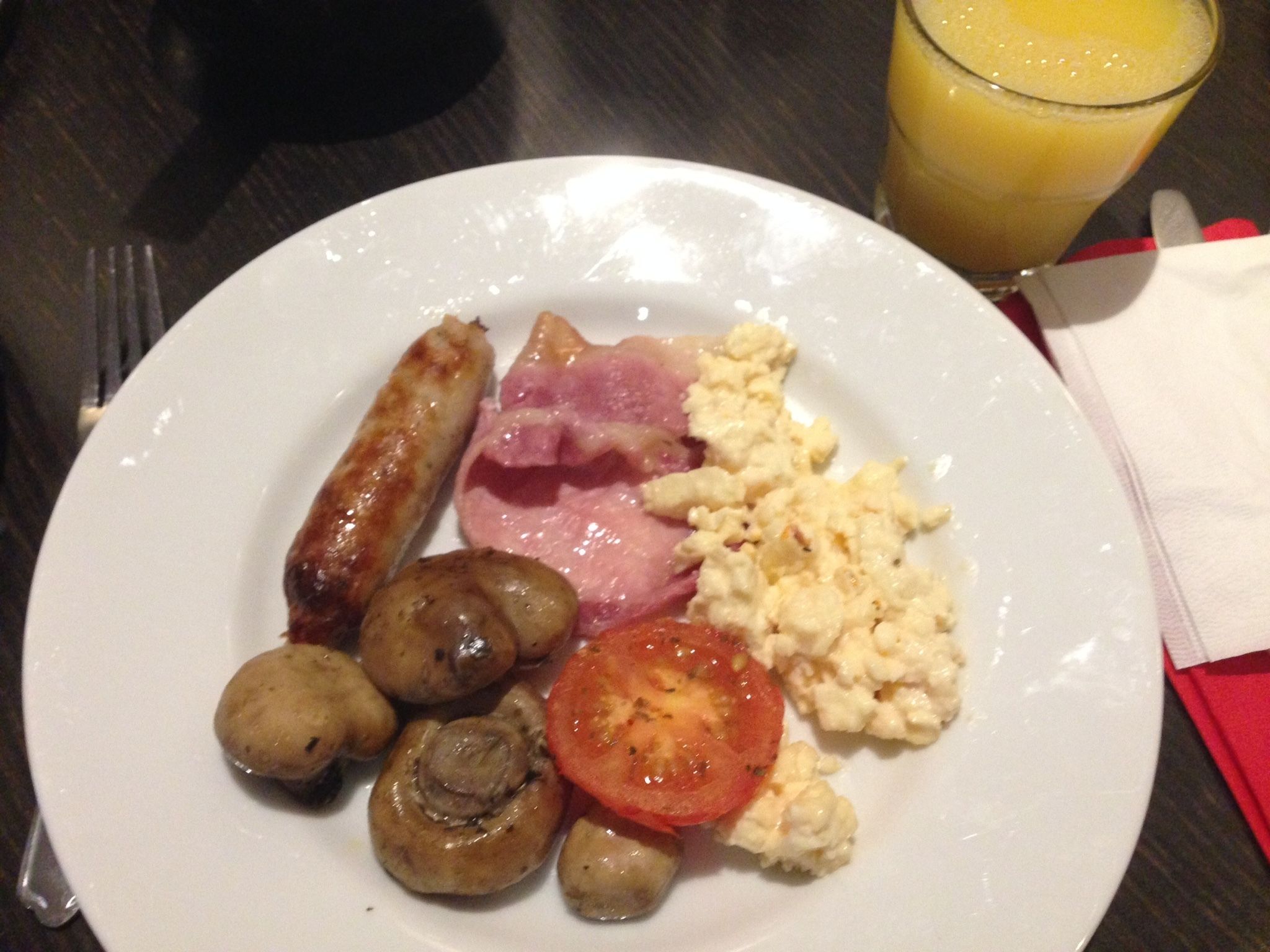 A plate with scrambled eggs, ham, sausages, mushrooms, and a tomato slice.