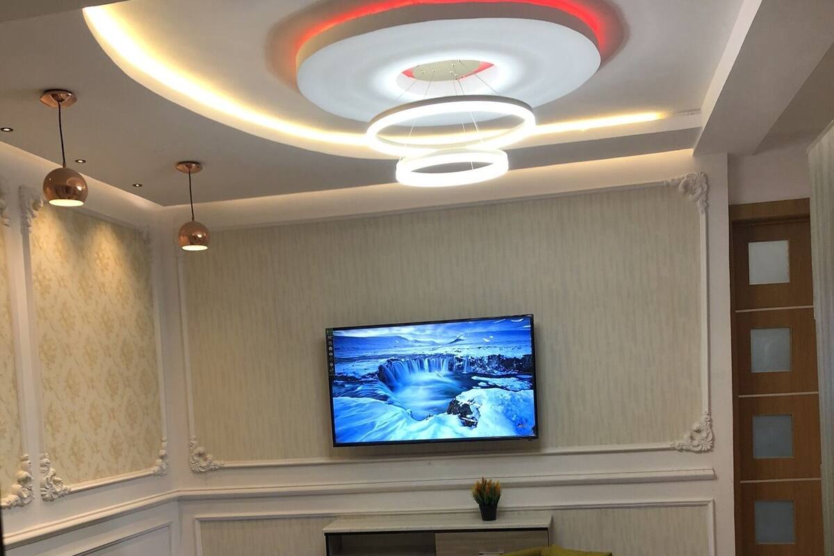 A modern living room with a flat-screen TV mounted on the wall, a black sofa, a green armchair, and a small round coffee table.