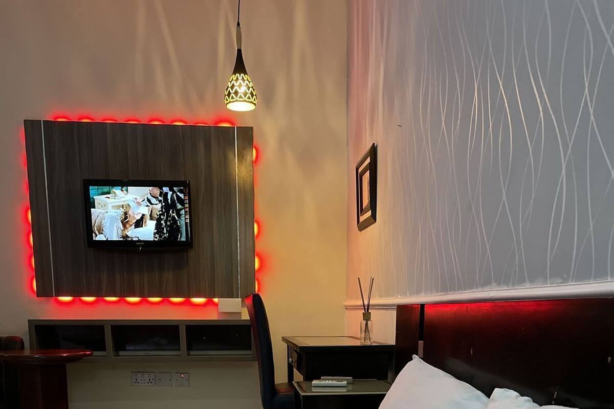 A hotel room with a bed, a TV mounted on the wall, a desk, and a chair.