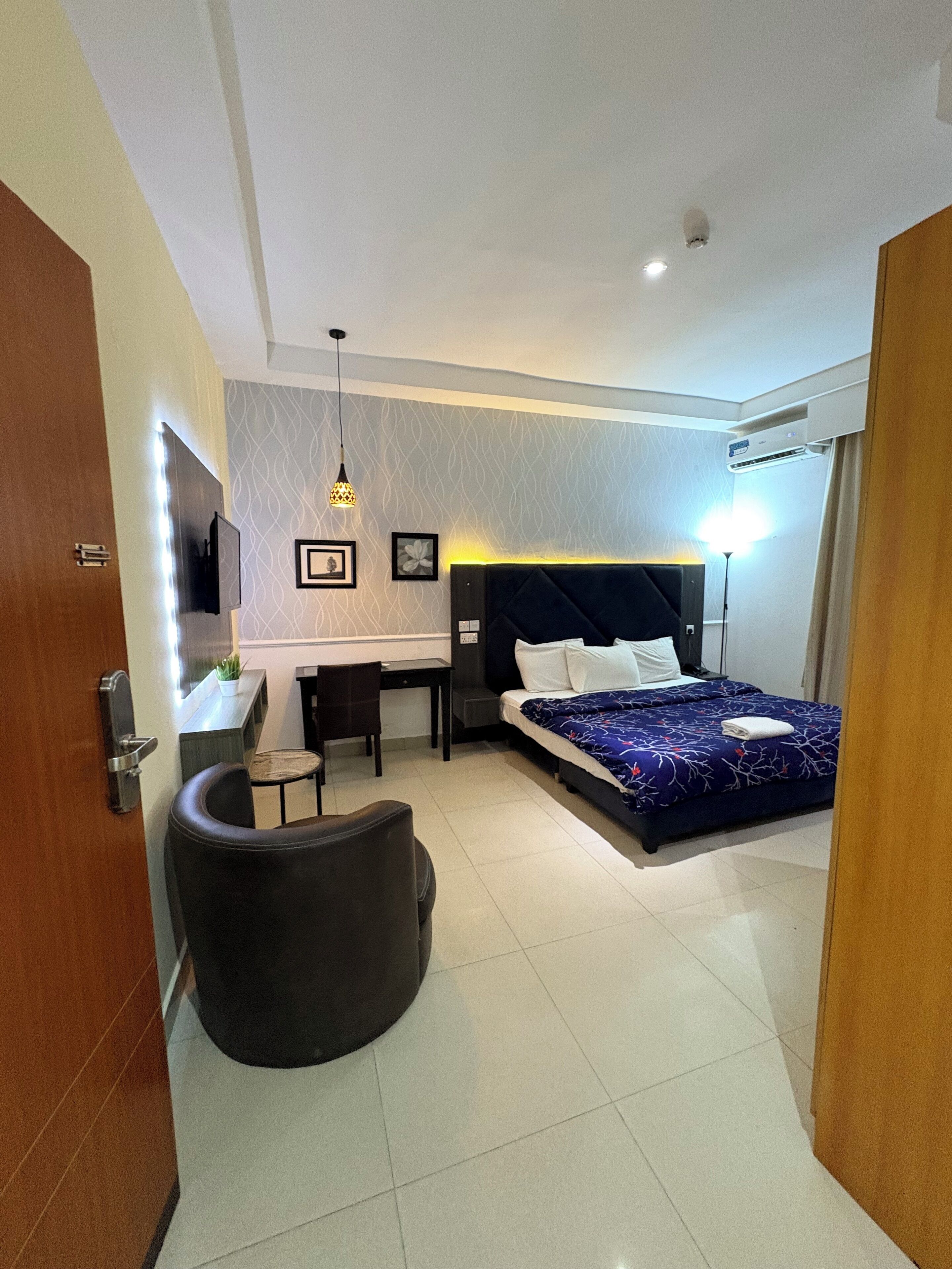 A modern hotel room with a bed, desk, chair, and a small seating area.