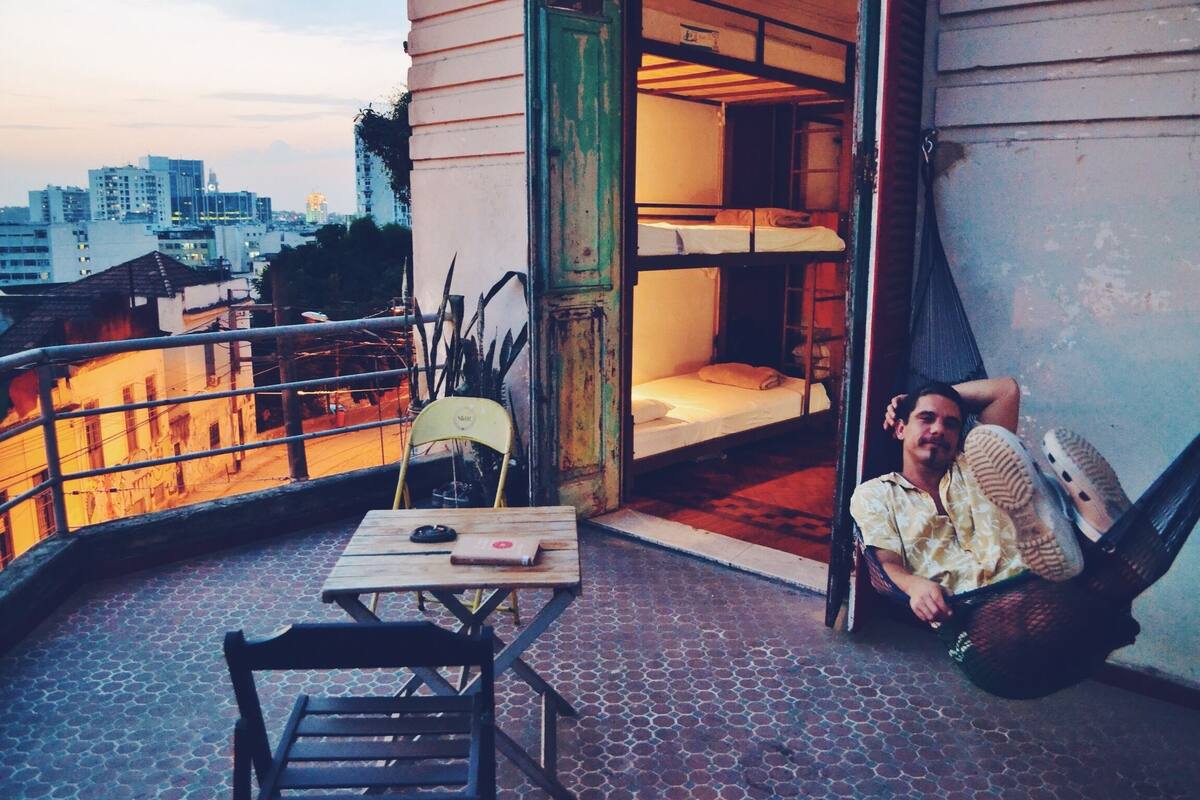 Ein Balkon mit Holztisch und -stühlen, einer Hängematte und einem Etagenbett mit Matratze und Kissen.